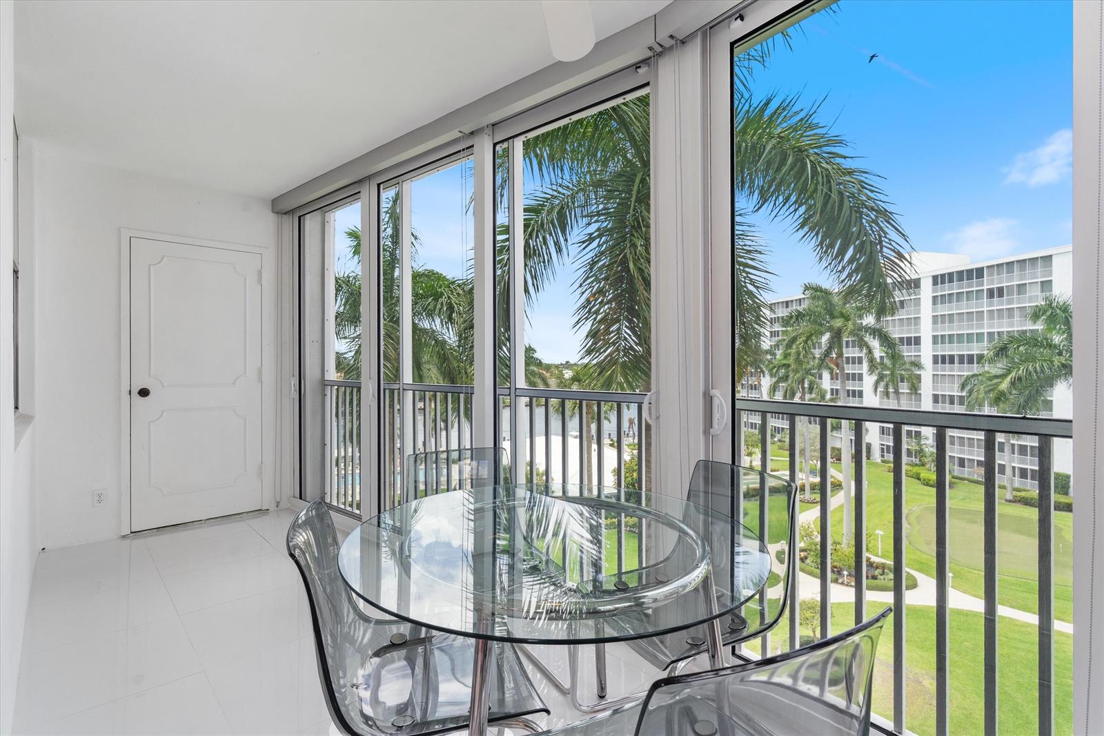 A sunroom features white tile floors, a glass dining table, and floor-to-ceiling windows overlooking palms — 3300 S Ocean Boulevard # c, Highland Beach FL 33487, HIGHLAND BEACH, FL