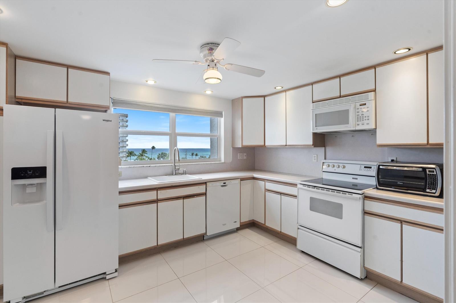 A white kitchen features light wood-trimmed cabinets, white appliances, and a window overlooking the ocean — 3300 S Ocean Boulevard # c, Highland Beach FL 33487, HIGHLAND BEACH, FL
