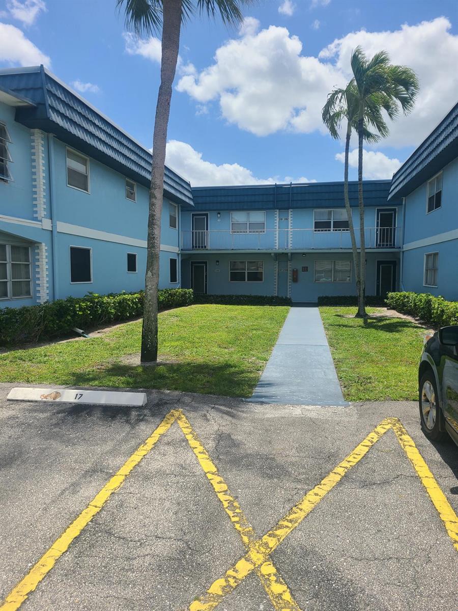 A two-story blue apartment building with a central courtyard and a paved walkway — 257 Brittany F # 257, Delray Beach FL 33446, DELRAY BEACH, FL