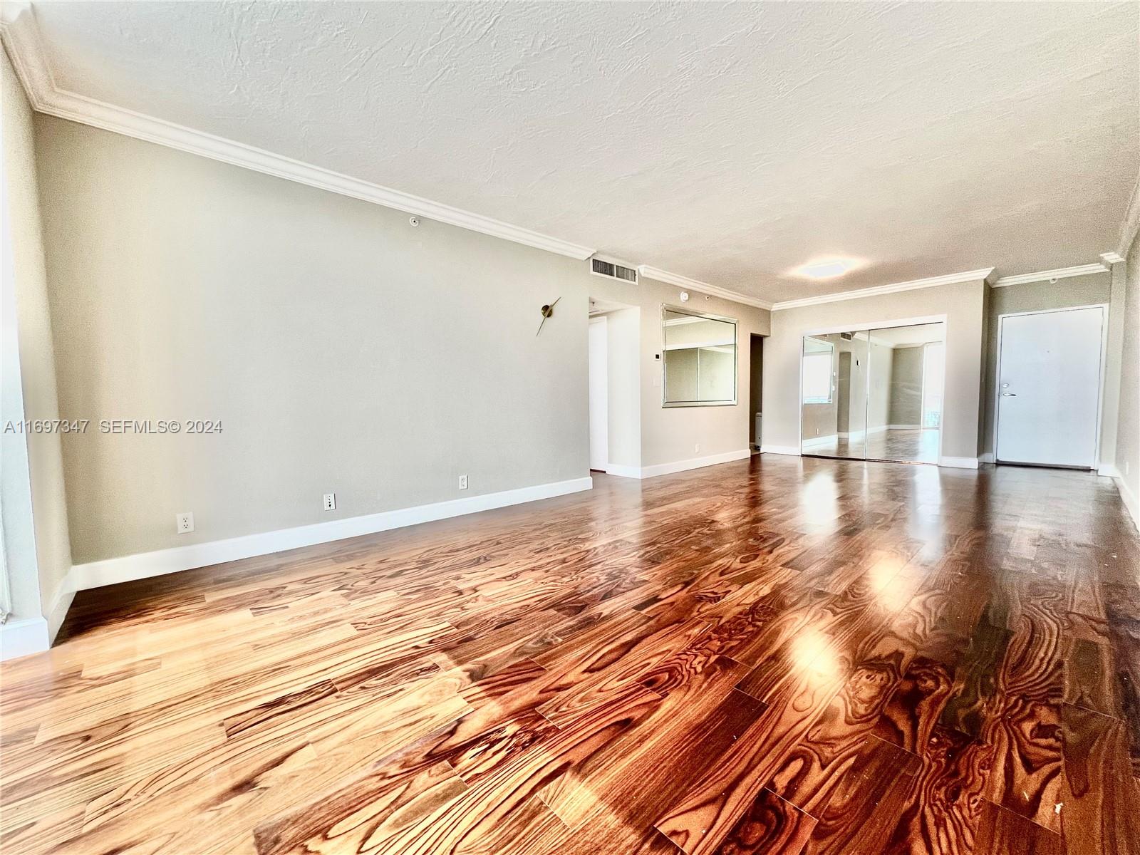 An empty room features dark wood-look flooring, light gray walls, and mirrored closet doors — 3000 S Ocean Dr # 1012, Hollywood FL 33019, HOLLYWOOD, FL