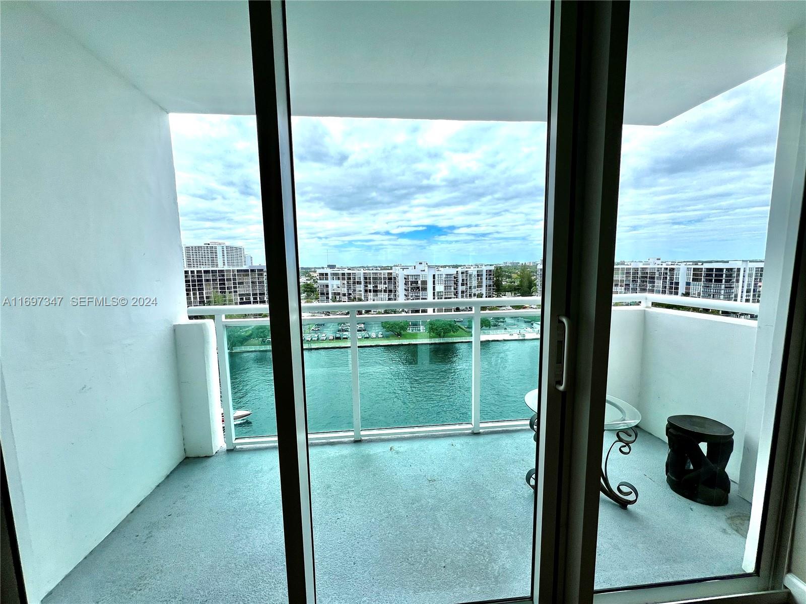 A balcony with a glass railing overlooks a waterway and apartment buildings — 3000 S Ocean Dr # 1012, Hollywood FL 33019, HOLLYWOOD, FL