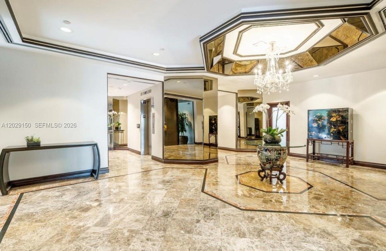 A marble-floored foyer features a crystal chandelier, mirrored walls, and a central decorative table — 151 SE 15th Rd # 502, Miami FL 33129, MIAMI, FL