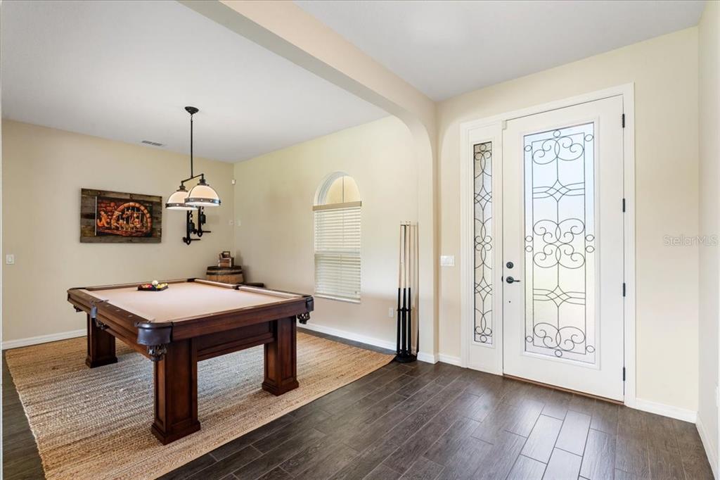 A room with a pool table, dark wood flooring, and a white front door — 3801 BOWFIN TRAIL, KISSIMMEE, FL