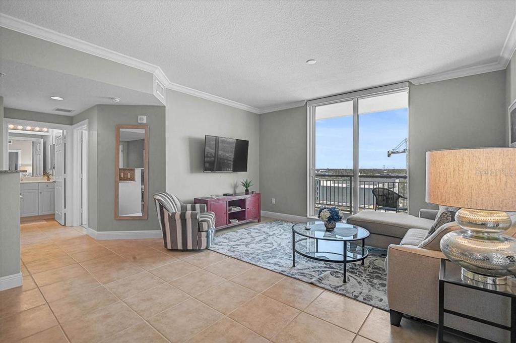 A living room features tile floors, a gray area rug, a balcony, and a television — 800 N TAMIAMI TRAIL UNIT 910, SARASOTA, FL