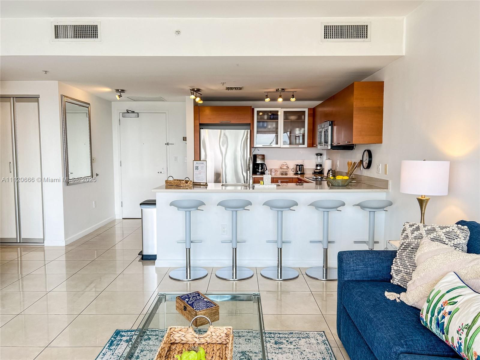 A kitchen with wood cabinets and a breakfast bar opens into a living area — 3250 NE 1st Ave # 708, Miami FL 33137, MIAMI, FL