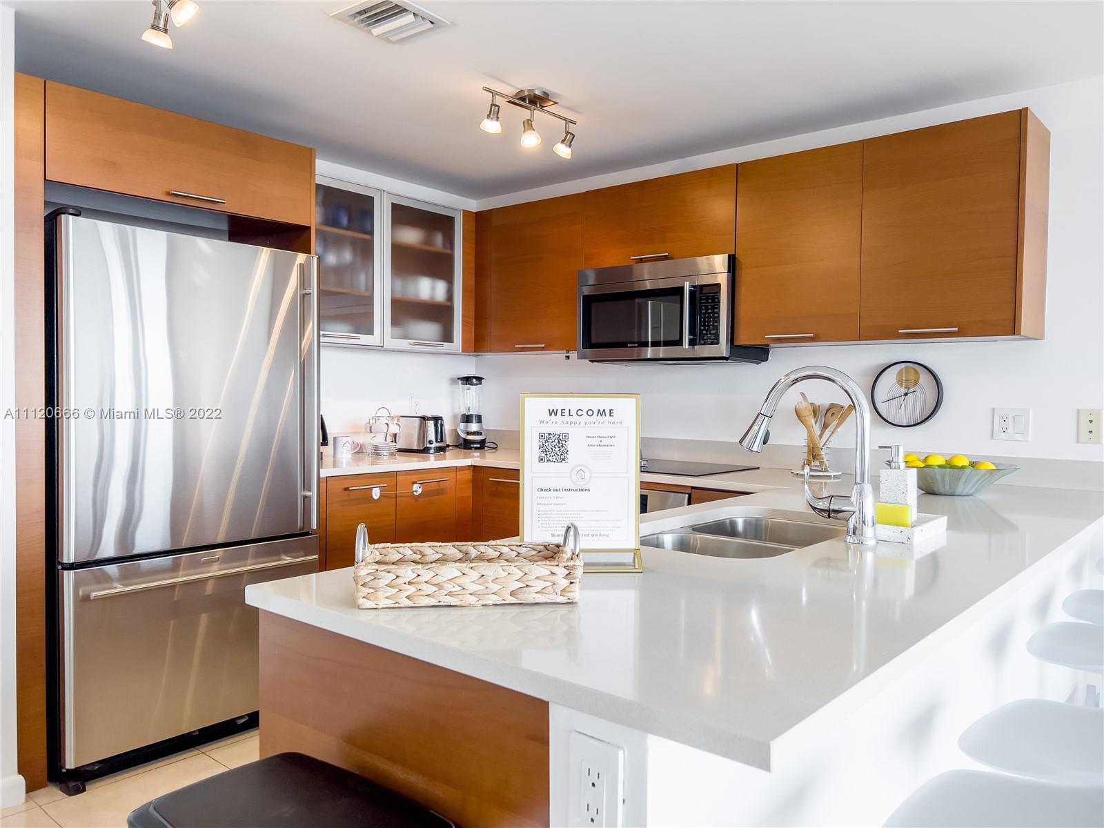 A modern kitchen features wood cabinets, stainless steel appliances, and a white quartz island countertop — 3250 NE 1st Ave # 708, Miami FL 33137, MIAMI, FL