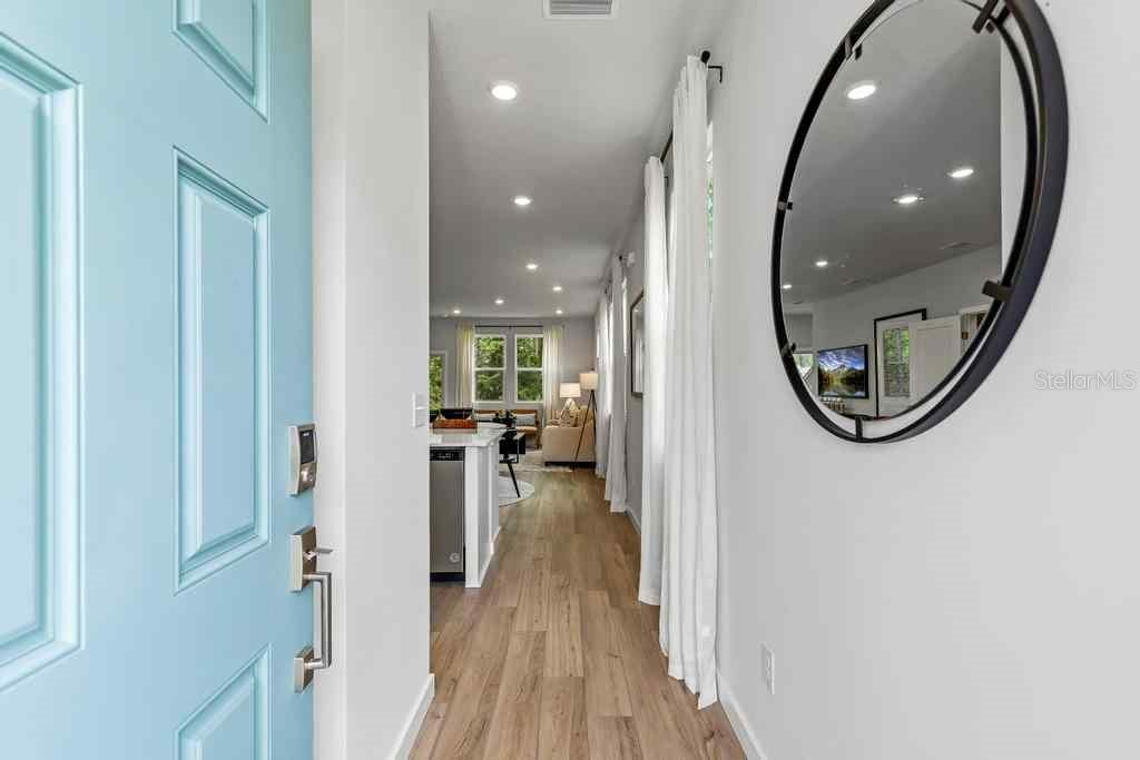 A light blue front door opens into a hallway with wood floors and a round mirror — 10723 WATERFIELD ROAD, JACKSONVILLE, FL