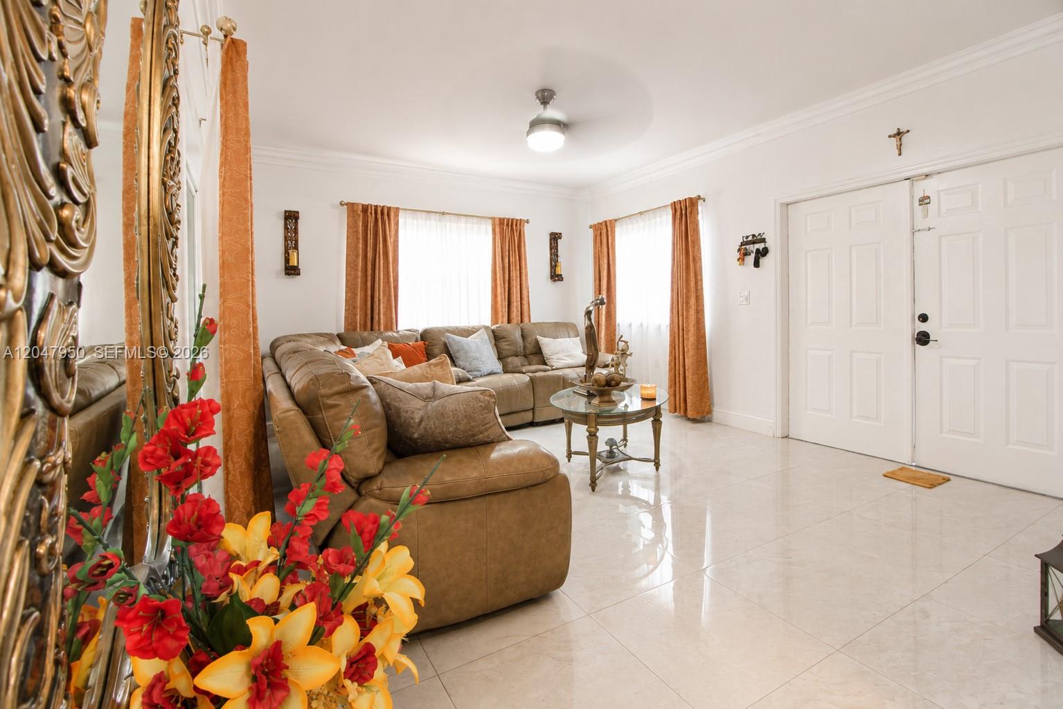 A living room features a brown leather sectional, tile flooring, and orange curtains — 1351 NE 41st Pl, Homestead FL 33033, HOMESTEAD, FL