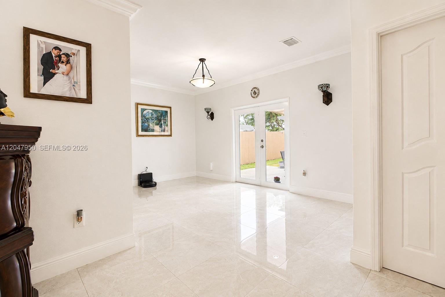 A bright, tiled room features a wedding portrait, wall sconces, and glass double doors — 1351 NE 41st Pl, Homestead FL 33033, HOMESTEAD, FL