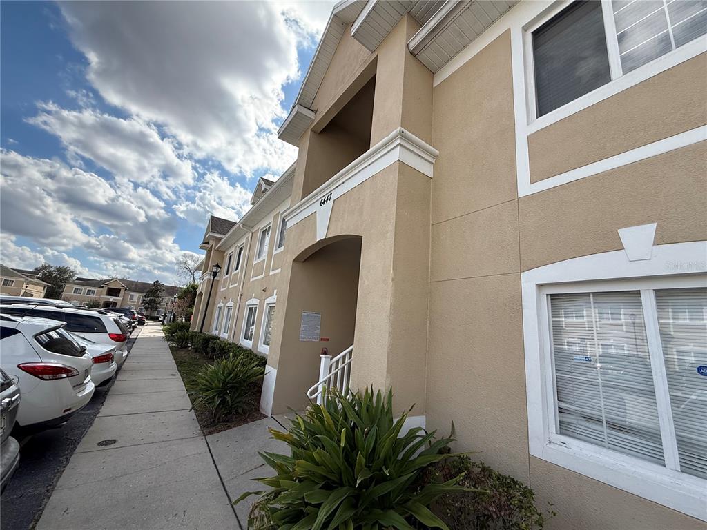 A multi-story apartment building exterior features tan stucco walls, white trim, and a sidewalk — 6447 CYPRESSDALE DRIVE UNIT 201, RIVERVIEW, FL