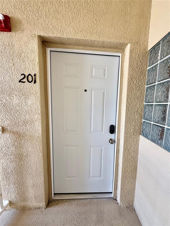 A white six-panel door with a digital lock is set into a textured beige wall — 6447 CYPRESSDALE DRIVE UNIT 201, RIVERVIEW, FL