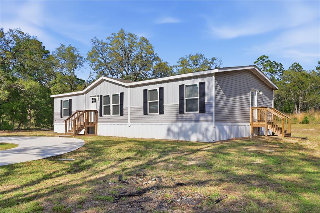 A single-story manufactured home with gray siding sits on a grassy lot with trees — 4959 SW 178TH TERRACE, DUNNELLON, FL