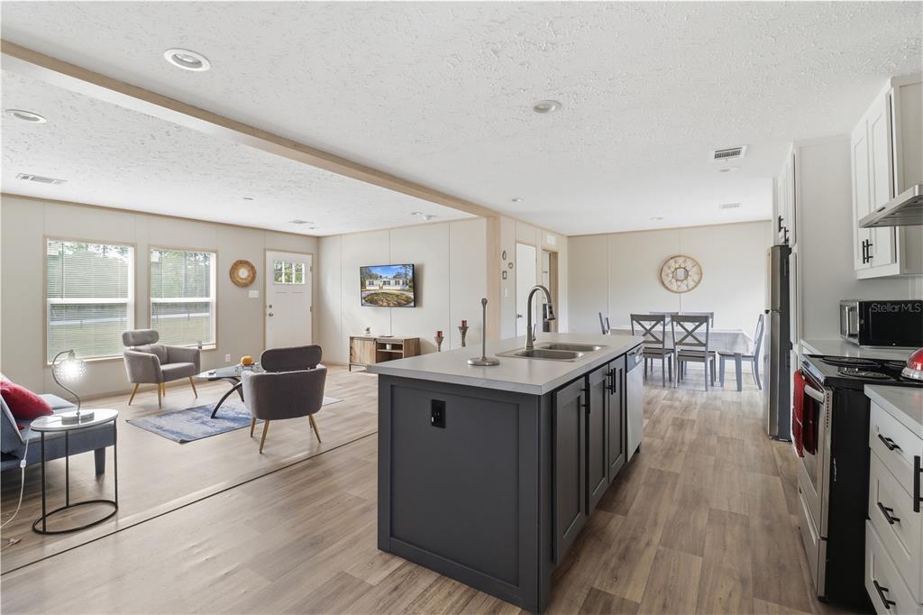 An open-concept kitchen with a dark gray island overlooks a living area and dining space — 4959 SW 178TH TERRACE, DUNNELLON, FL