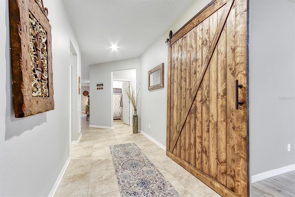 A hallway features tile flooring, a large wooden barn door, and wall-mounted decor — 5611 BARLETTA DRIVE, ST CLOUD, FL