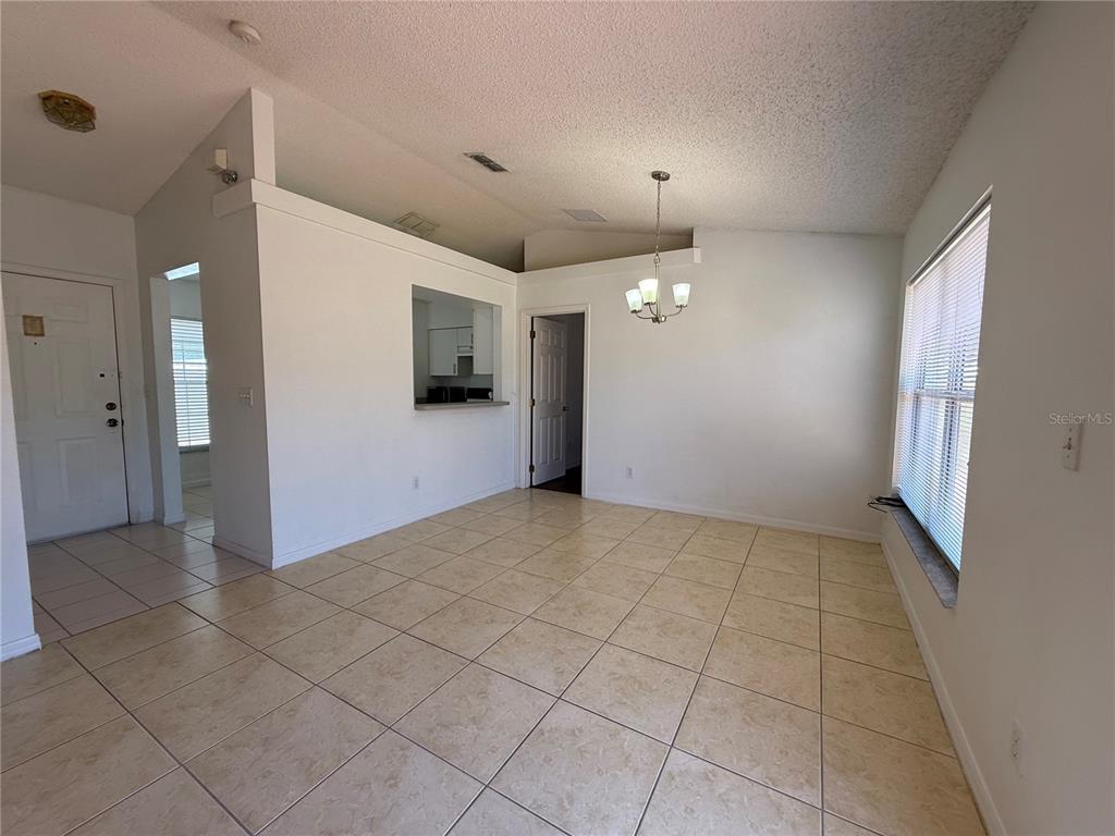 A dining area with beige tile flooring, a vaulted ceiling, and a kitchen pass-through window — 11755 FOXGLOVE DRIVE, CLERMONT, FL