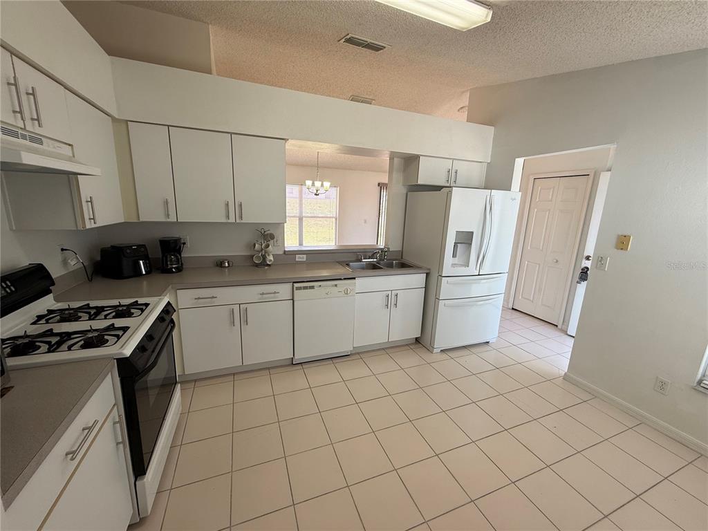 A kitchen features white cabinets, white appliances, a tiled floor, and a pass-through window — 11755 FOXGLOVE DRIVE, CLERMONT, FL