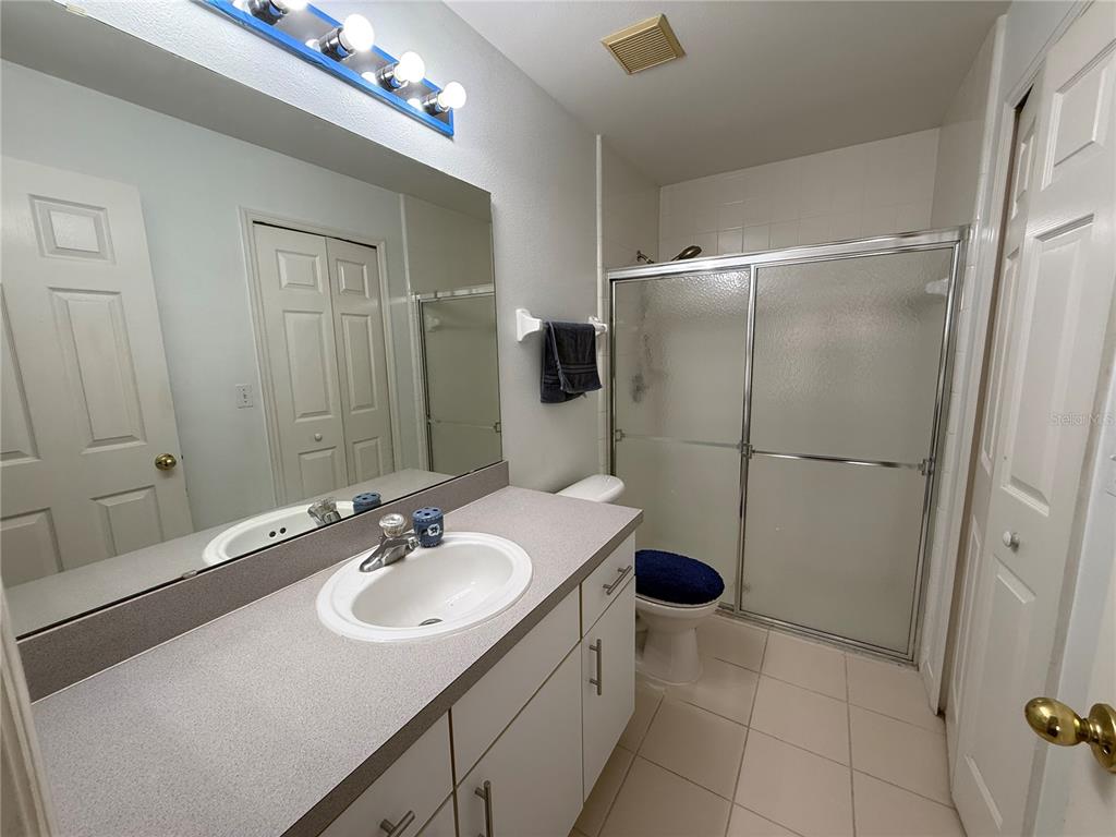 A bathroom features a vanity with a gray countertop, a mirror, and a glass-enclosed shower — 11755 FOXGLOVE DRIVE, CLERMONT, FL