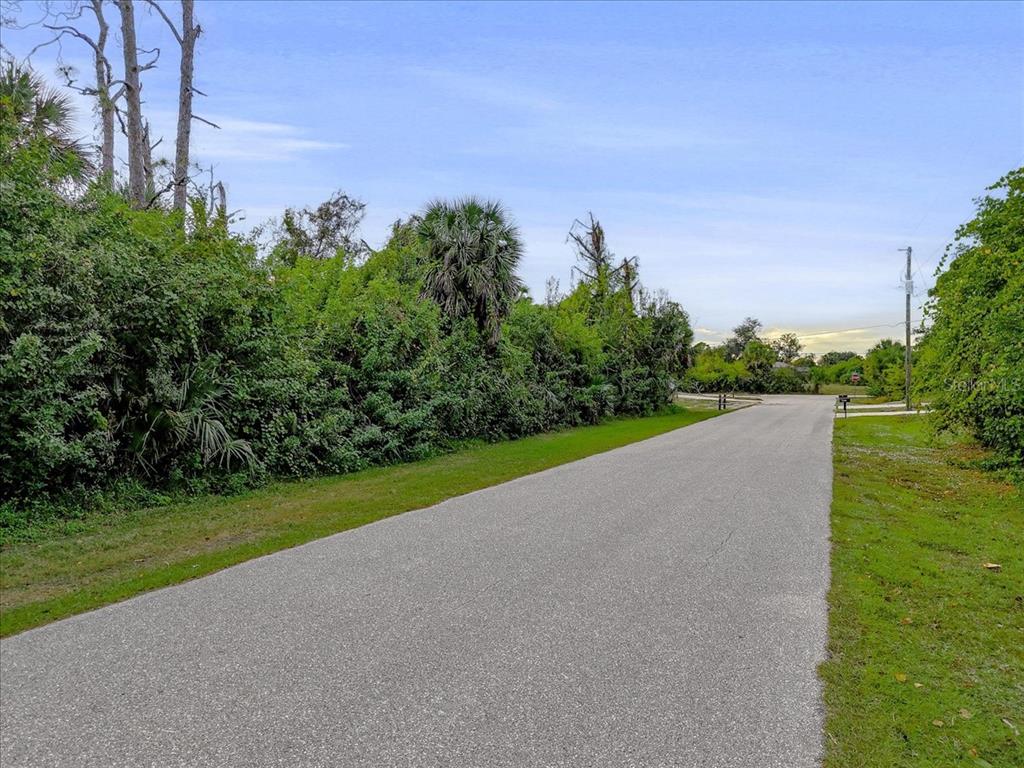 A paved road winds past a dense line of trees and shrubs under a blue sky — 11947 HELICON AVENUE, PORT CHARLOTTE, FL