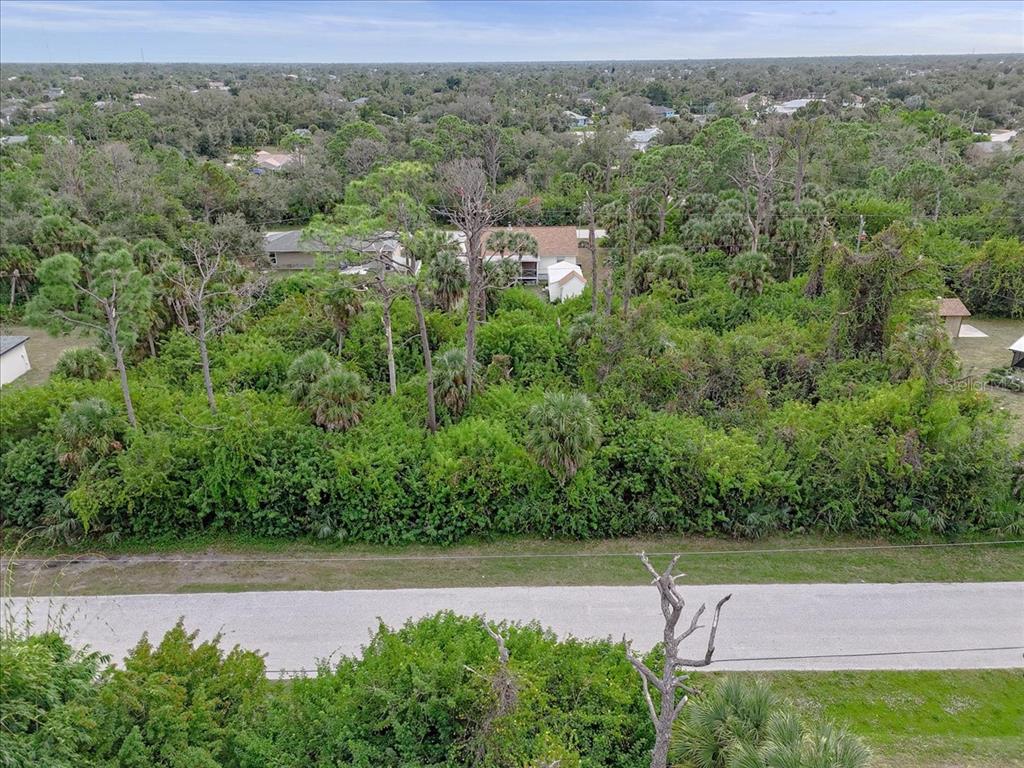 An aerial view shows a densely wooded vacant lot bordered by a paved road — 11947 HELICON AVENUE, PORT CHARLOTTE, FL