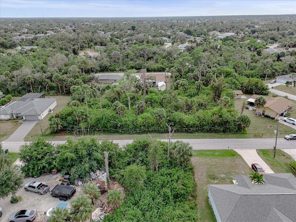 An aerial view shows a vacant, wooded residential lot situated between two existing houses — 11947 HELICON AVENUE, PORT CHARLOTTE, FL