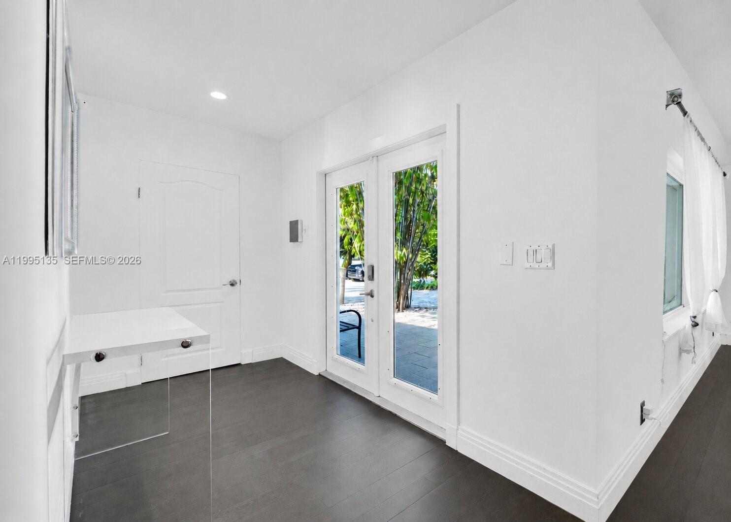 A bright entryway features dark wood flooring, white walls, a white console table, and glass doors — 1895 NE 118th Rd, North Miami FL 33181, NORTH MIAMI, FL