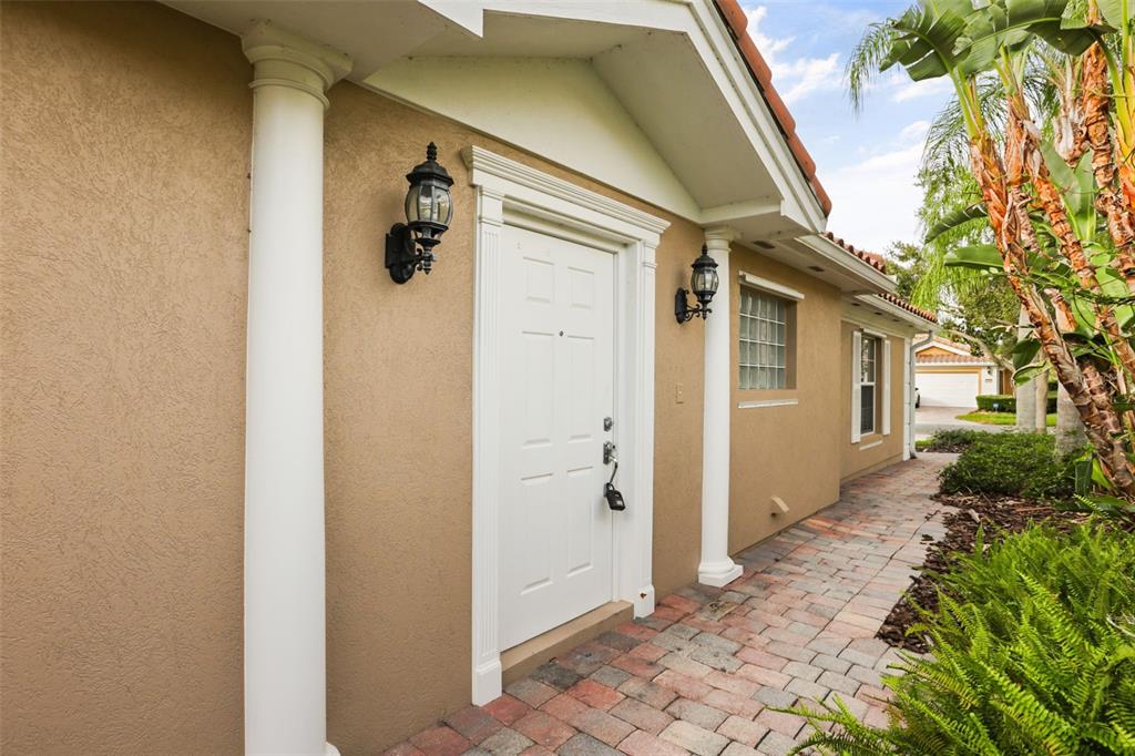 A white front door with a lockbox sits between two columns on a paved walkway — 11972 KAJETAN LANE, ORLANDO, FL