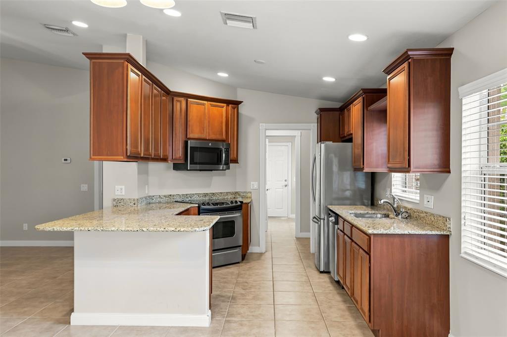 A kitchen features wood cabinets, granite countertops, stainless steel appliances, and tile flooring — 11972 KAJETAN LANE, ORLANDO, FL