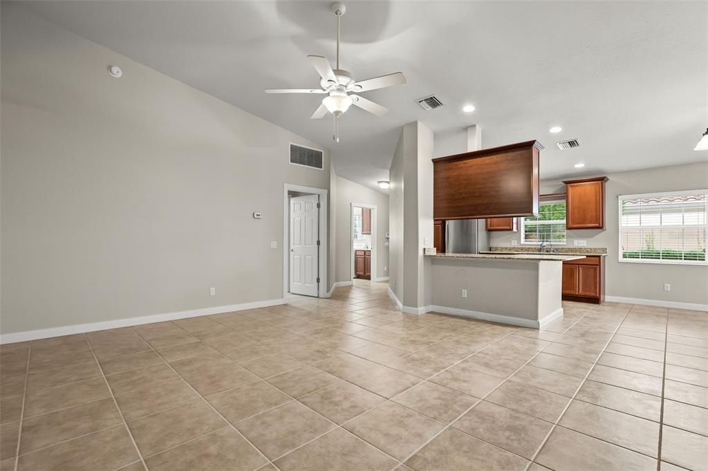 A spacious living area with tile flooring leads into an open kitchen with wooden cabinets — 11972 KAJETAN LANE, ORLANDO, FL