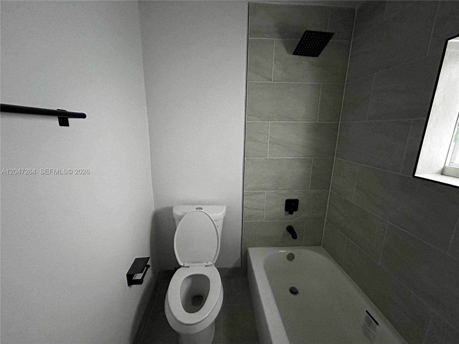A bathroom features a white toilet, a tiled bathtub surround, and matte black fixtures — 4429 SW 21st St, West Park FL 33023, WEST PARK, FL