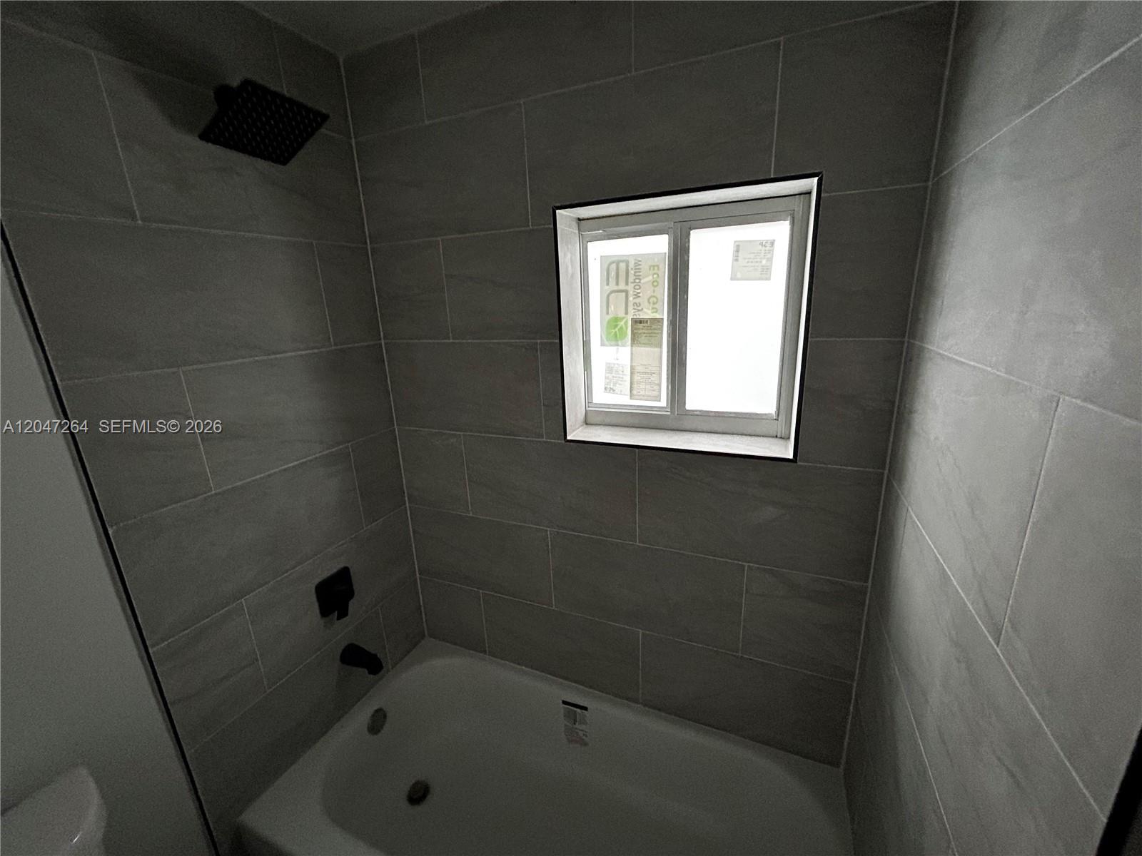 A bathroom features a bathtub with a showerhead and gray tiled walls around a window — 4429 SW 21st St, West Park FL 33023, WEST PARK, FL