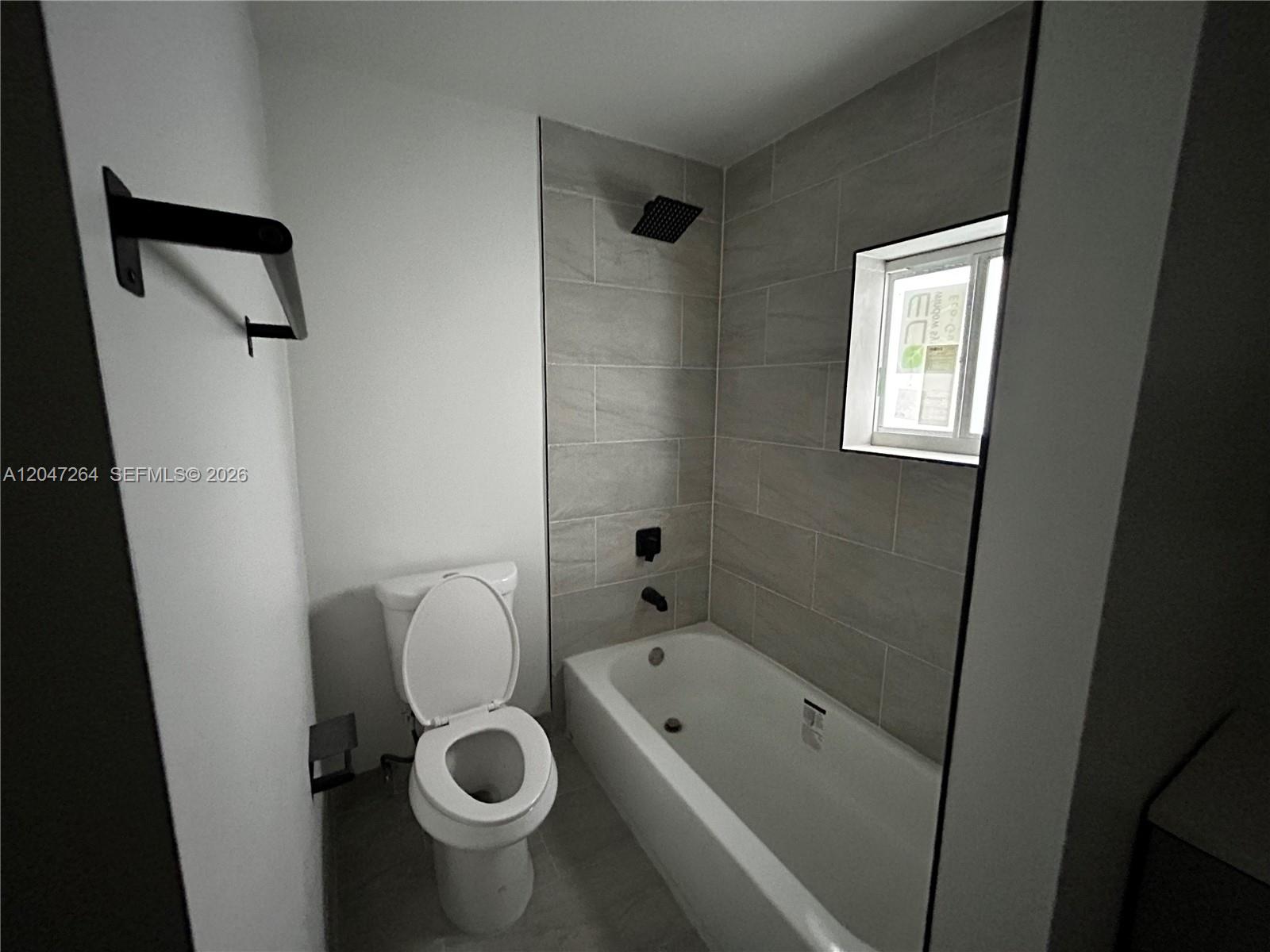 A bathroom features a white toilet, a bathtub with a shower head, and tiled walls — 4429 SW 21st St, West Park FL 33023, WEST PARK, FL