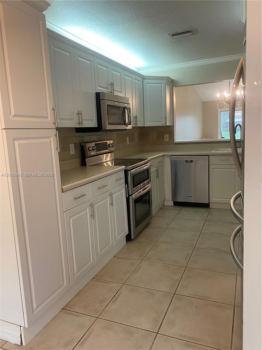 A kitchen features white cabinets, stainless steel appliances, and light-colored tile flooring — 803 SW 119th Way, Davie FL 33325, DAVIE, FL