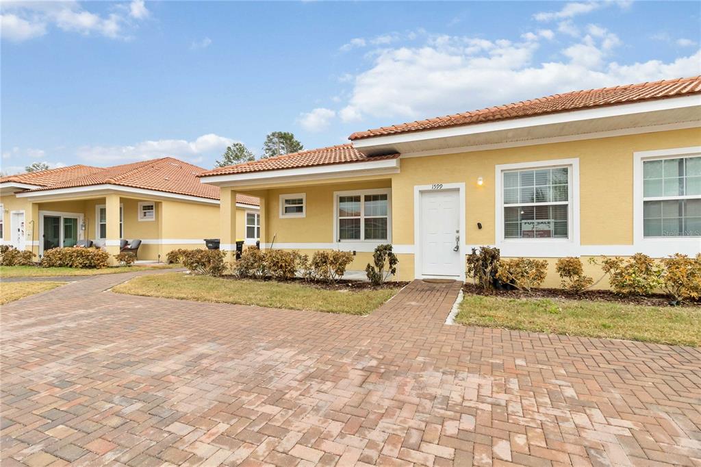 A yellow one-story house with a tiled roof and a brick paver driveway — 1599 CUMIN DRIVE UNIT 1599, KISSIMMEE, FL