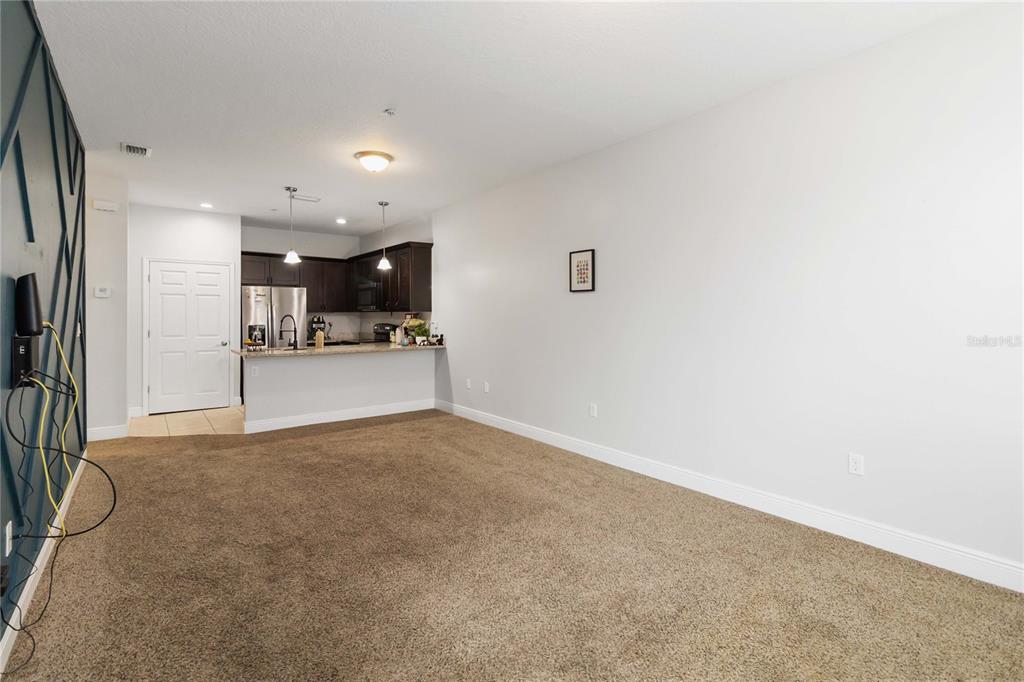 An open-concept living area features brown carpeting, a kitchen with dark cabinets, and a breakfast bar — 1599 CUMIN DRIVE UNIT 1599, KISSIMMEE, FL