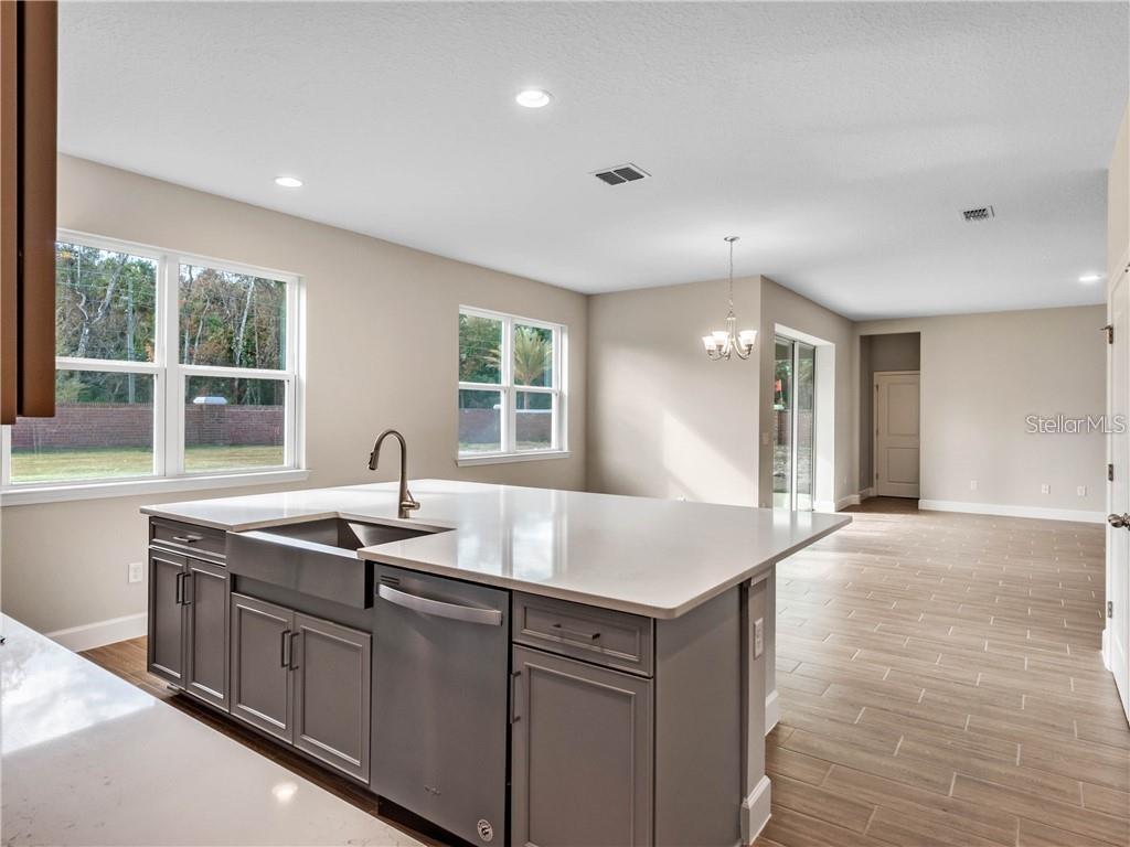 A kitchen island with a farmhouse sink and gray cabinets overlooks an open dining area — 913 TALON PLACE, WINTER SPRINGS, FL