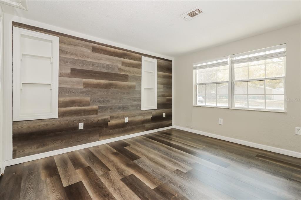 An empty room features wood-look plank flooring and an accent wall with built-in shelving — 3147 36TH AVENUE N, ST PETERSBURG, FL