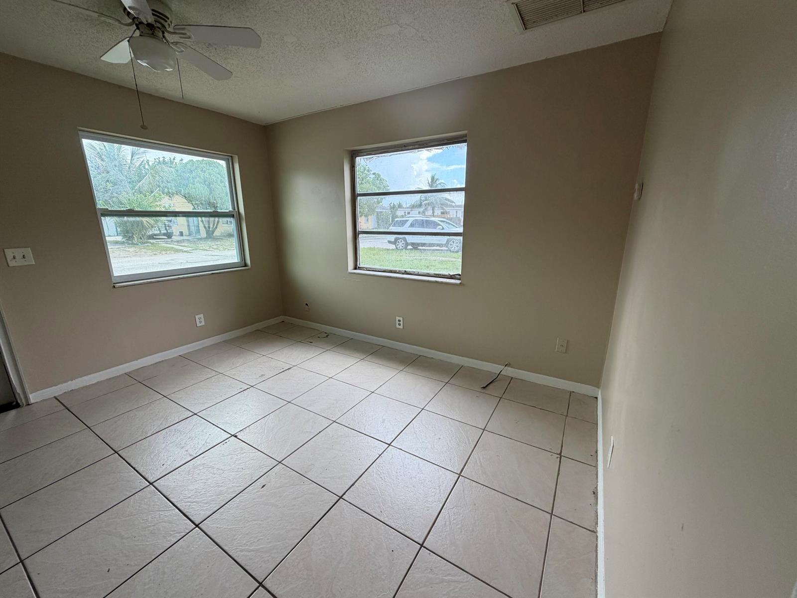 An empty room features beige walls, large square floor tiles, and two windows — 3654 Coconut Road, Palm Springs FL 33461, PALM SPRINGS, FL