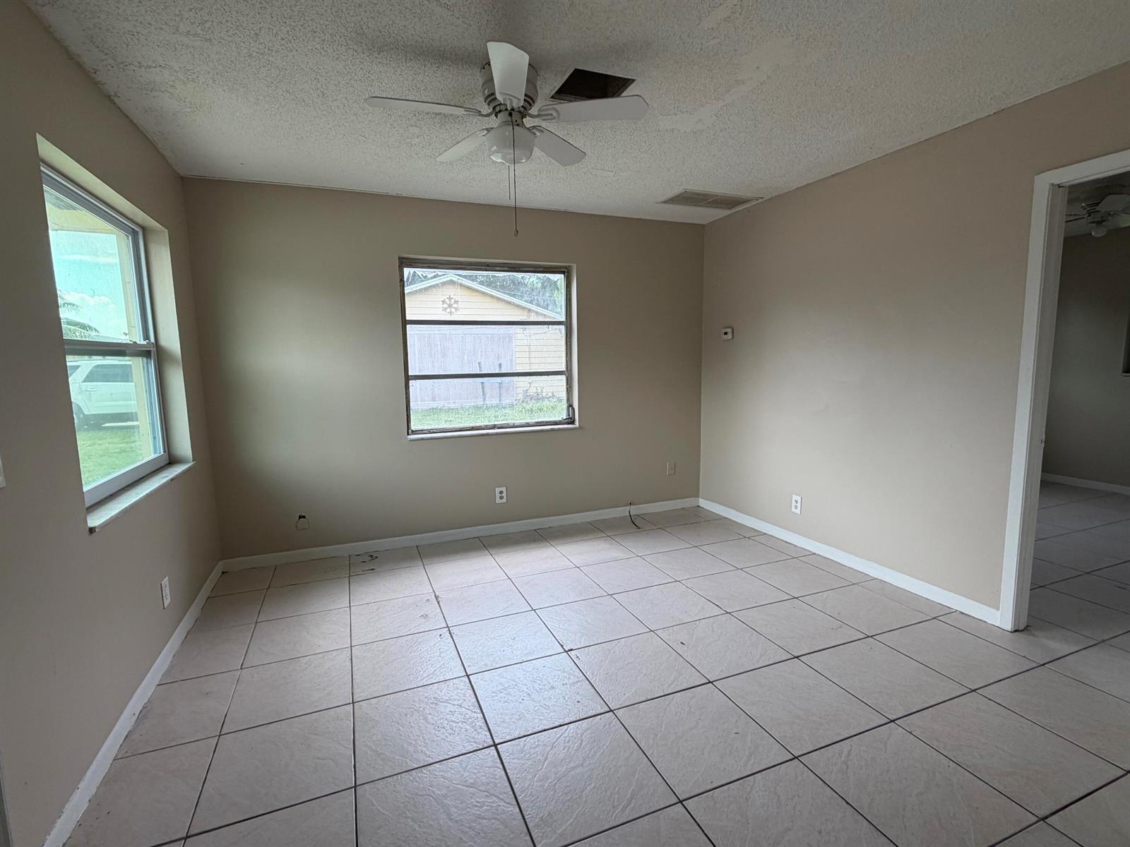 An empty room with beige walls, tiled flooring, a ceiling fan, and two windows — 3654 Coconut Road, Palm Springs FL 33461, PALM SPRINGS, FL