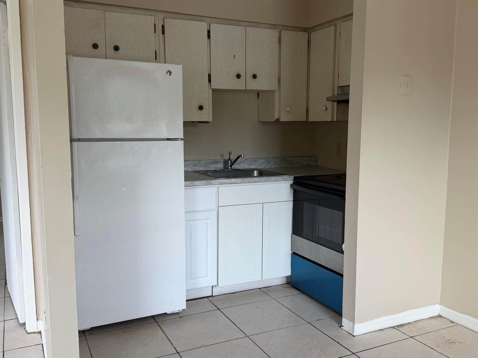 A small kitchen features white cabinets, a white refrigerator, a sink, and a black stove — 3654 Coconut Road, Palm Springs FL 33461, PALM SPRINGS, FL