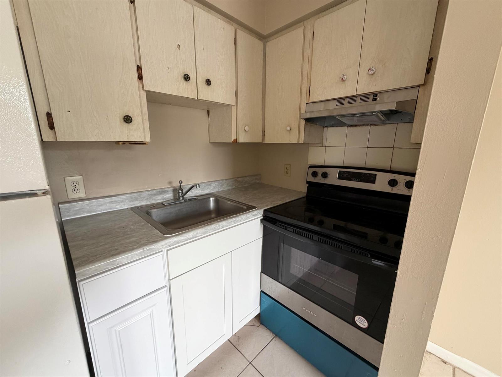 A small kitchen features white cabinets, a stainless steel sink, and a black electric range — 3654 Coconut Road, Palm Springs FL 33461, PALM SPRINGS, FL