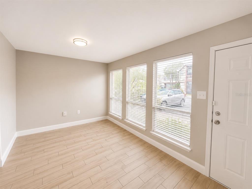 An empty room with light wood-look tile flooring, three large windows, and a white door — 3922 CRAYRICH CIRCLE UNIT C-4, ORLANDO, FL