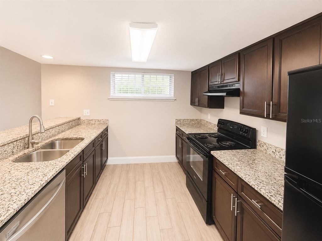 A kitchen features dark wood cabinets, granite countertops, stainless steel appliances, and light wood flooring — 3922 CRAYRICH CIRCLE UNIT C-4, ORLANDO, FL