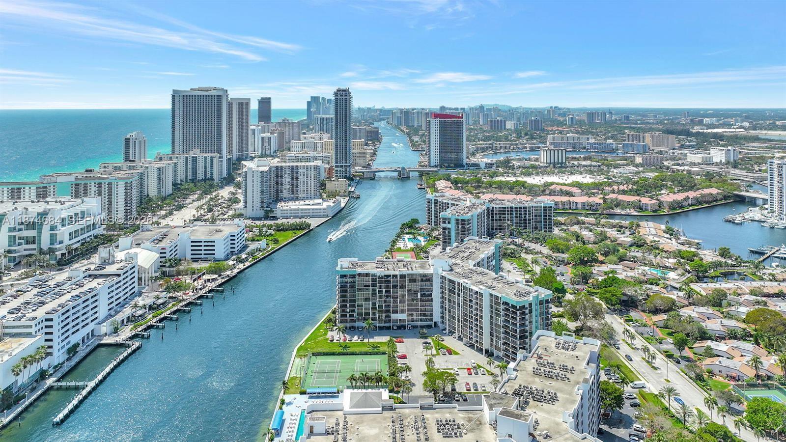 An aerial view shows a waterway lined with high-rise apartment buildings and a tennis court — 1000 Parkview Dr # 805, Hallandale Beach FL 33009, HALLANDALE BEACH, FL