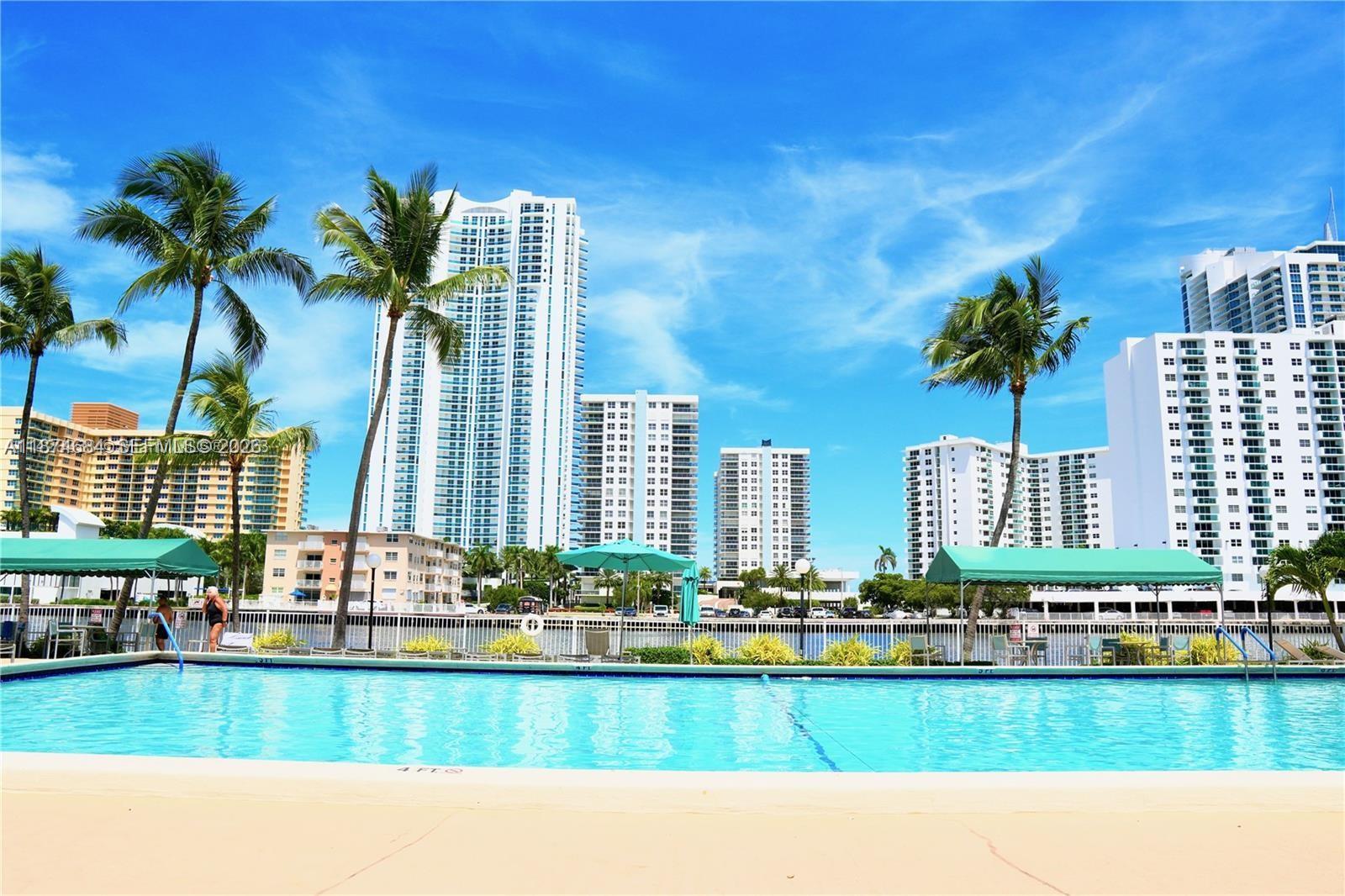 A swimming pool sits in the foreground with tall residential buildings and palm trees behind it — 1000 Parkview Dr # 805, Hallandale Beach FL 33009, HALLANDALE BEACH, FL