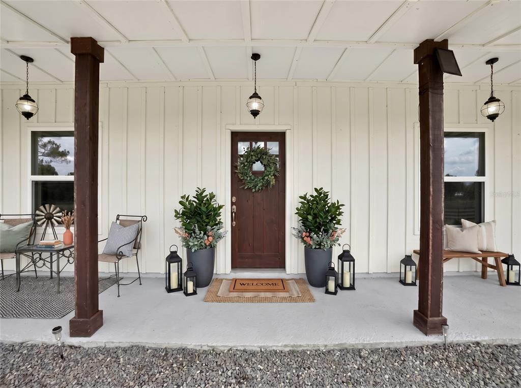 A covered front porch features a dark wood door, two large planters, and wooden pillars — 13009 NW 123RD PLACE, ALACHUA, FL