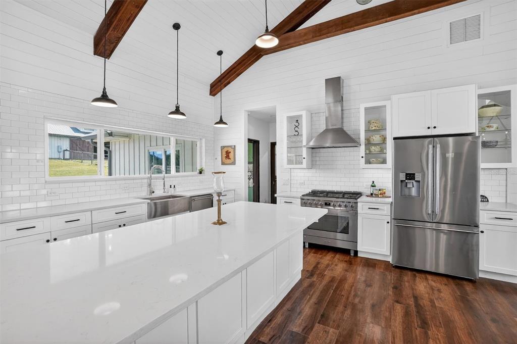 A modern kitchen features white cabinetry, a large island, subway tile, and exposed wood beams — 13009 NW 123RD PLACE, ALACHUA, FL
