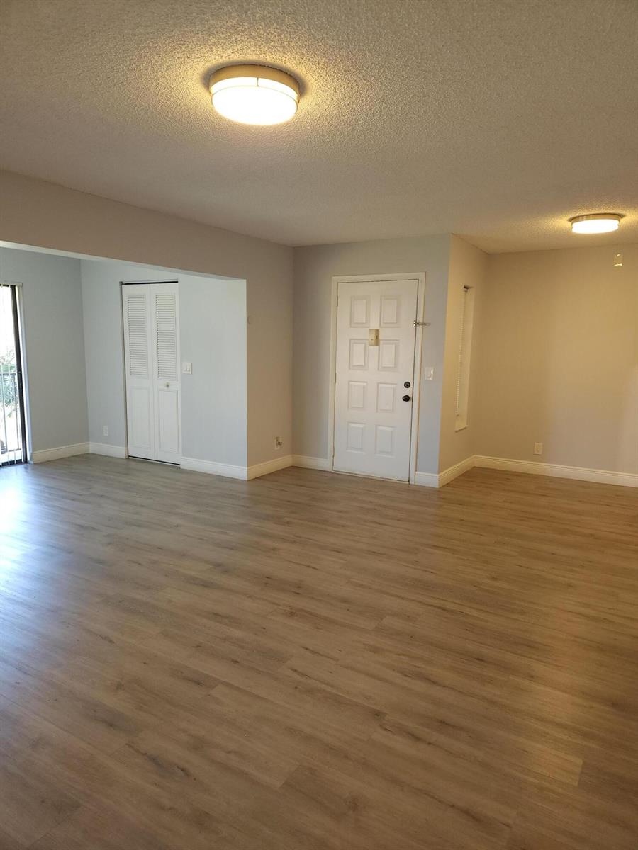 An empty living room features light wood-look flooring, white walls, and two ceiling light fixtures — 502 Shady Pine Way # D2, FL 33415, FL