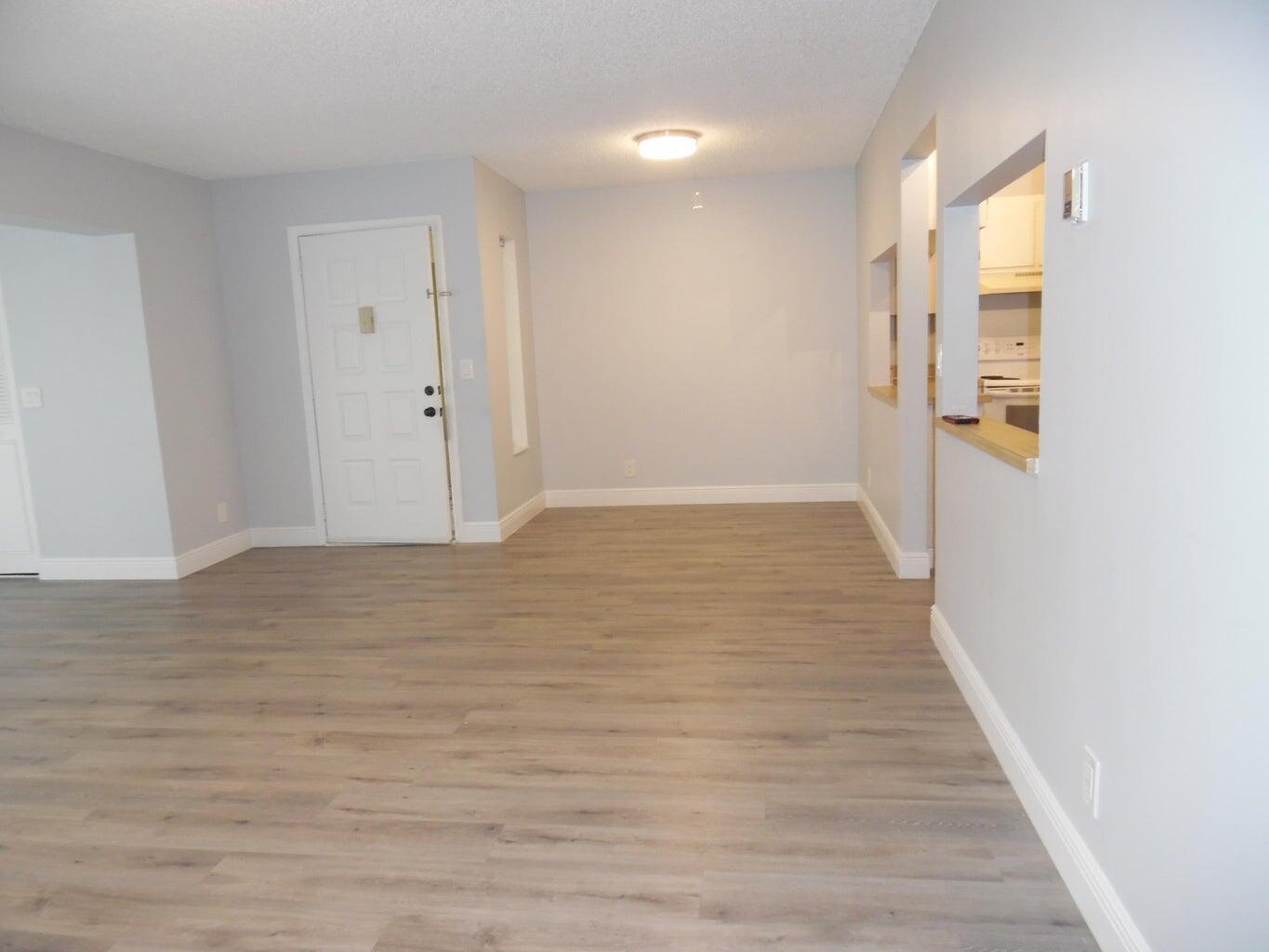 An empty room with light gray walls, wood-look flooring, and a kitchen pass-through window — 502 Shady Pine Way # D2, FL 33415, FL