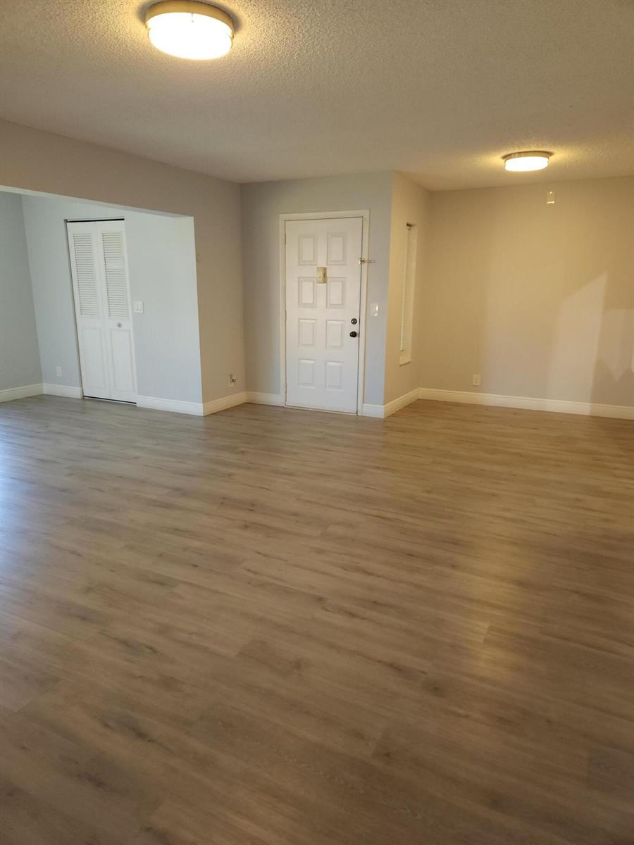 An empty room features light wood-look flooring, white walls, and two ceiling-mounted light fixtures — 502 Shady Pine Way # D2, FL 33415, FL