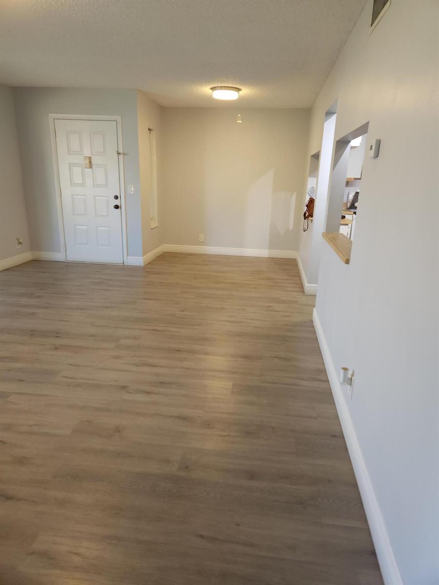 An empty room with light wood-look flooring, gray walls, and a white entry door — 502 Shady Pine Way # D2, FL 33415, FL